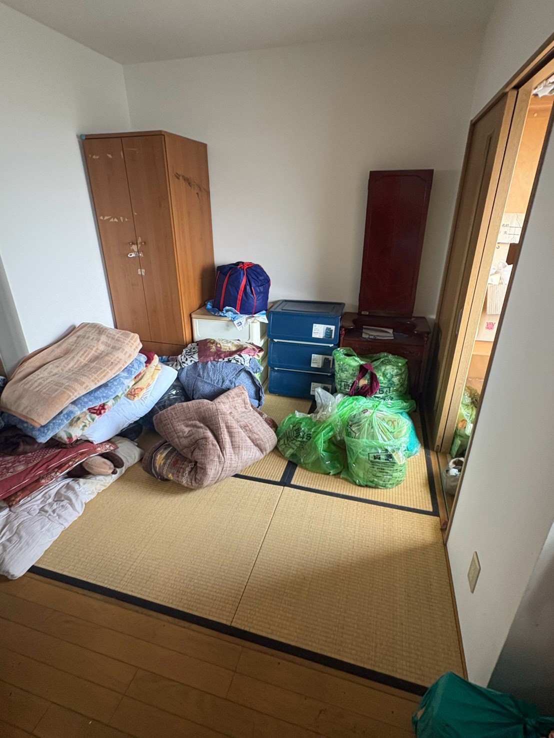 布団や衣類、収納ケースなどが置かれた作業前の和室